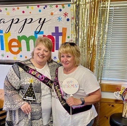 two smiling women holding happy retirement signs